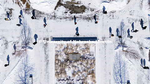 Aerial view of students crossing campus in the snow. Students cast shadows on the snow covered sidew