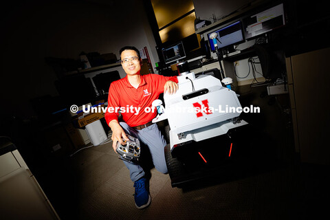 Qiang Liu, assistant professor in the School of Computing, poses next to a small vehicle used by the