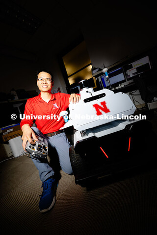 Qiang Liu, assistant professor in the School of Computing, poses next to a small vehicle used by the