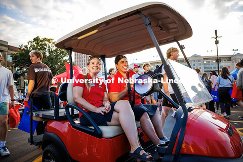 Staff members Hollie Swanson (left) and Kalan Walters drive a golf cart through the Big Red Welcome 