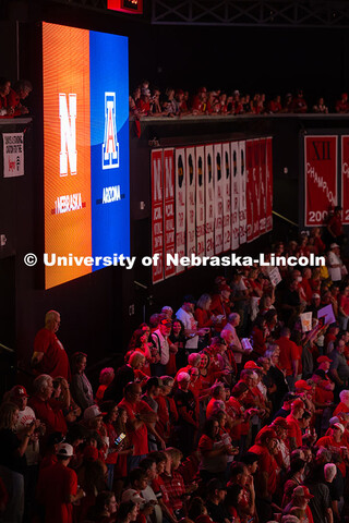 Husker fans are bathed in red light from the scoreboard before the start of the volleyball game. Neb