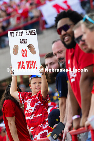 Grayden Gadeken holds up a sign that reads "My first Husker game, Go Big Red!" He and his parents ca