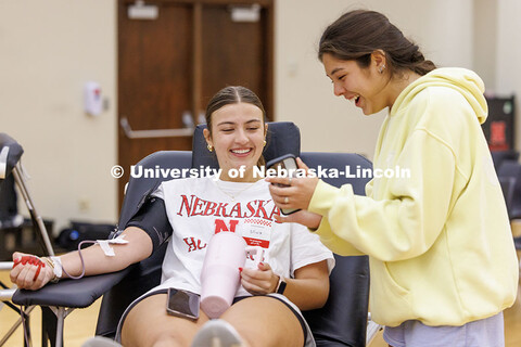 Olivia Burgess, left, looks at Ella Glaser’s phone as she gives blood during the 2025 Homecoming B