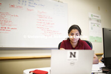 Young woman at a computer with a marker board full of equations behind her. Raikes school photo shoo