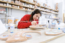 Senior Alex Napolitano works on glazing her gecko serving platter for a ceramics course inside Richa