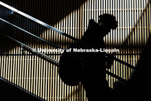 A student is silhouetted as sunlight shines on the wall behind them as they walk downstairs in the C