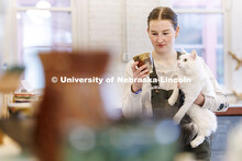 Kat Kastens, junior, looks at a cup while holding her cat Leo during the UNL Clay Club sale inside R