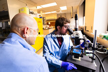 Brennan Watts, a fourth-year doctoral student, looks through a microscope at a checkerboard-patterne