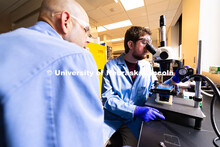 Brennan Watts, a fourth-year doctoral student, looks through a microscope at a checkerboard-patterne