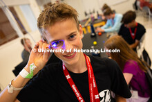 Austin Vaughan holds a blue LED light connected to a small battery up to his eye during an engineeri