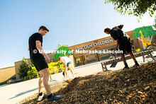 First-year students Glazier Demma, Kevin O'Connor and Winner Mutoke shovel mulch onto landscaping in