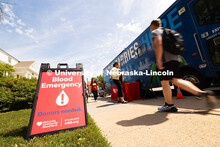 Students walk by a sign on the grass in front of a Nebraska Community Blood Bank bus that reads "Blo