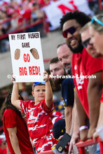 Grayden Gadeken holds up a sign that reads "My first Husker game, Go Big Red!" He and his parents ca