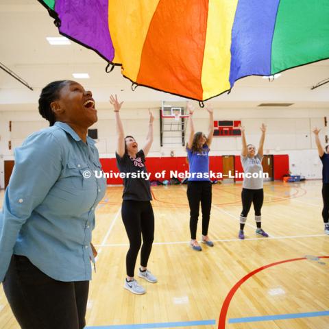 Tanika Cooper, left, reacts as the students watch the parachute float back to the floor. Masters students in TEAC 893 Seminar Workshop in Health & Physical Education apply learning principals to physical education games in Mabel Lee hall gymnasium. 