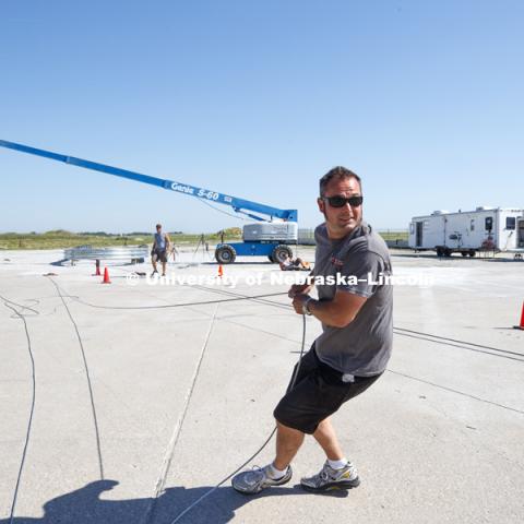 Alex Russell, a testing and maintenance technician, who has worked at the facility for 22 years since completing his undergrad degree, stretches the cable to get out the slack before it is attached to the test truck. The boom in the background will be used to film the test from overhead. Test of bull-nose barrier for use in medians to protect cars from overpass columns. Test was at university's Midwest Roadside Safety Facility at the Lincoln airport. June 5, 2018. Photo by Craig Chandler / University Communication.