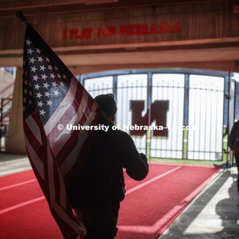 Jerod Post, '13 and a Marine veteran, carries the US flag into Memorial Stadium to the starting point of the Ruck March. Beginning of veterans Ruck March which uses Nebraska and Iowa veterans to carry the game ball from Lincoln to Iowa City. November 14, 2018. Photo by Craig Chandler / University Communication.