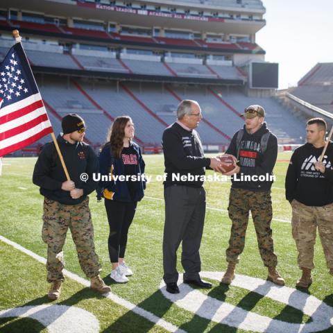 Jerod Post, '13 and a Marine veteran, and undergraduate Natalie Kraft, a Navy veteran, watch as Athletic Director Bill Moos presents the game ball to undergraduate and Marine veteran Jake Post. At right is undergraduate and Army veteran Jared Collins. Beginning of veterans Ruck March, which uses Nebraska and Iowa veterans to carry the game ball from Lincoln to Iowa City. November 14, 2018. Photo by Craig Chandler / University Communication.