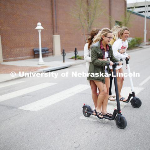 Four students roll onto campus riding electric scooters. April 22, 2019. Photo by Craig Chandler / University Communication.