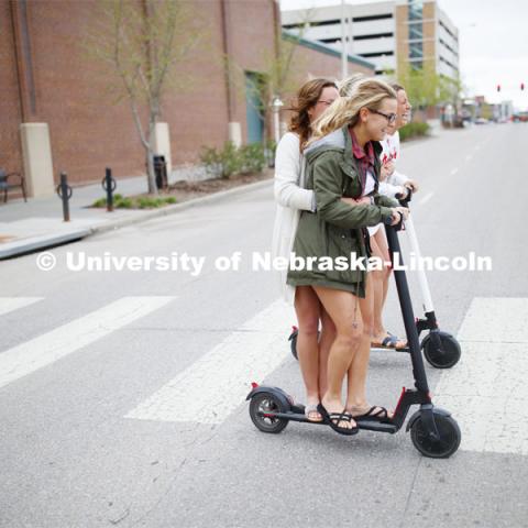 Four students roll onto campus riding electric scooters. April 22, 2019. Photo by Craig Chandler / University Communication.