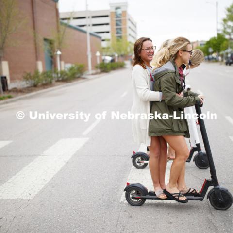 Four students roll onto campus riding electric scooters. April 22, 2019. Photo by Craig Chandler / University Communication.