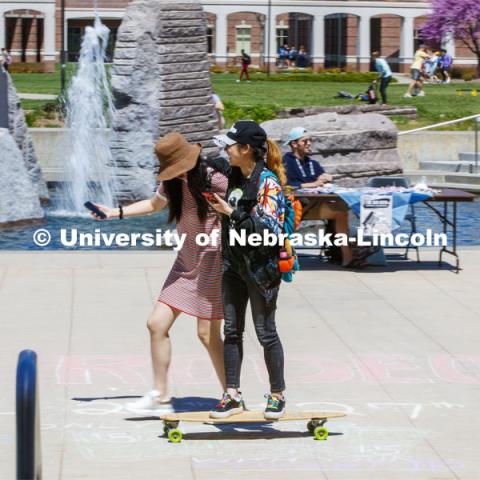 Hanchen Zhang gets a free ride on her skateboard as her friend, Sihui Li walks her along the plaza by the fountain. April 24, 2019. Photo by Craig Chandler / University Communication.