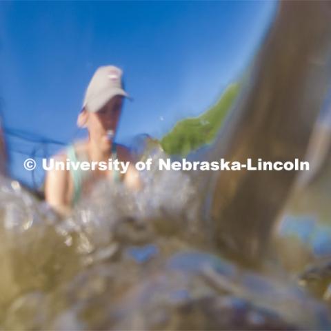 Kayla Vondracek, junior in Environmental Studies, fights the current and depth to take a sand sample as she researches algae in the Niobrara River. Jessica Corman, assistant professor in the School of Natural Resources, UCARE research group researching algae in the Niobrara River. Fort Niobrara National Wildlife Refuge. July 12, 2019. Photo by Craig Chandler / University Communication.