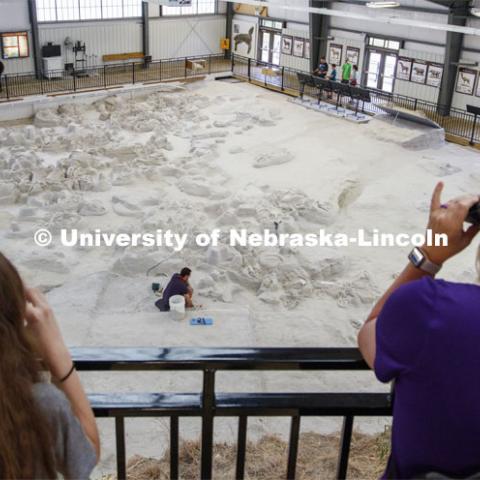 Visitors watch from an observation deck as Raymond Dierdorf, an intern at the park, removes layers of ash over a rhino skull. Ashfall Fossil Beds State Historical Park in north central Nebraska. August 2, 2019. Photo by Craig Chandler / University Communication.