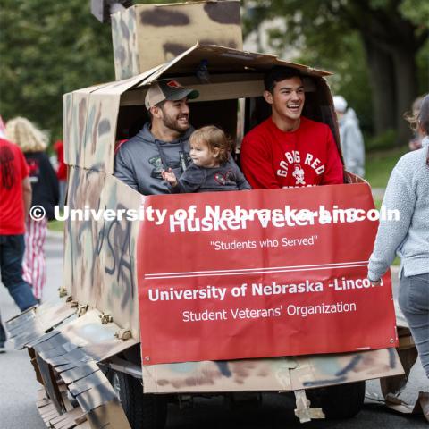 Lorelai Dingman, 2, shares a ride with Marine veterans and second year students Rodrigo Venegas, left, and Jessi Meyer share the back of the Student Veterans' Organization golf cart decorated as a tank. Cornstock celebration and Homecoming Parade. October 4, 2019. Photo by Craig Chandler / University Communication.