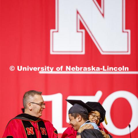 Hector de Jesus Palala Martinez is hugged by Marshall Marianna Banks as he receives his degree from Chancellor Ronnie Green. Graduate Commencement and Hooding at the Pinnacle Bank Arena. December 20, 2019. Photo by Craig Chandler / University Communication.