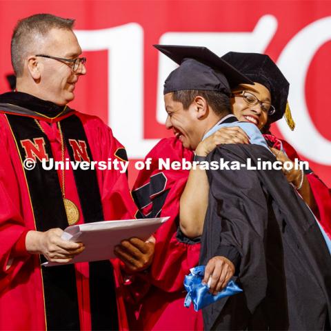 Hector de Jesus Palala Martinez is hugged by Marshall Marianna Banks as he receives his degree from Chancellor Ronnie Green. Graduate Commencement and Hooding at the Pinnacle Bank Arena. December 20, 2019. Photo by Craig Chandler / University Communication.