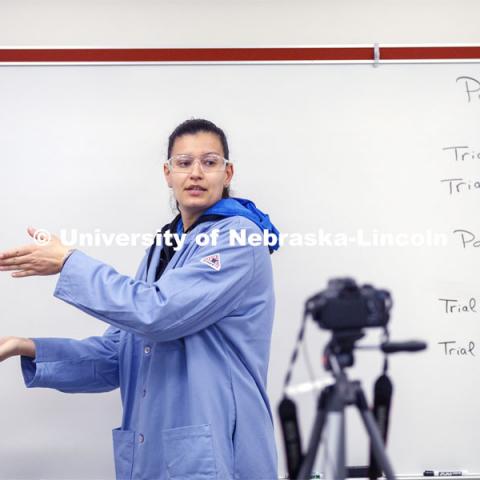 Jessica Periago, chemistry department lab manager, gestures to the side of the frame where the PowerPoint slides will appear as she records a Chem 110 lab on entropy and spontaneity. As a result of the Corona virus, Faculty are recording Chemistry labs in Hamilton Hall to prepare for the start of remote learning. March 24, 2020. Photo by Craig Chandler / University Communication.