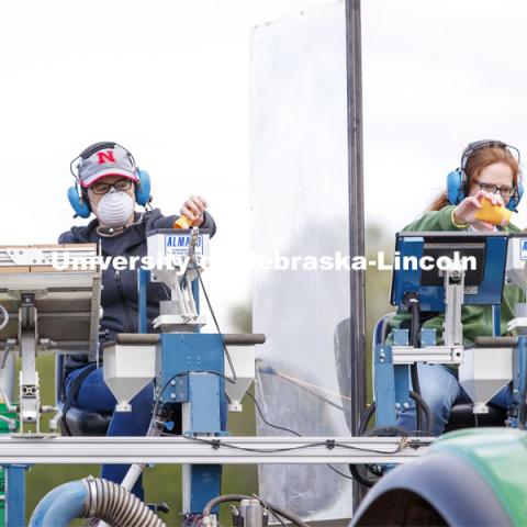 Brandi Sigmon and Christine Smith pours a packet of seeds into the hopper as the tractor slowly travels the field. James Schnable corn research group plants at agronomy fields at 84th and Havelock in northeast Lincoln. Schnable’s lab studies grain DNA to find the best varieties for breeding and genetic modification to help with traits including yields and drought resistance. The 2.5-acre plot was being planted with 752 genotypes in 1680 precisely randomized plots. To plant those plots along with a check genotype, the researchers used 1860 packets of seeds manually poured into a hopper every 7 seconds while sitting atop a custom research planter. May 6, 2020. Photo by Craig Chandler / University Communication.