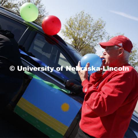 Ratch O'Connell blows up a blue balloon to decorate his vehicle.  Blue, yellow and green balloons and streamers, the national colors of Rwanda, along with Husker Red decorated many of the vehicles. Christ Place Church families gave the Rwandan students a vehicle parade to help celebrate the graduates and undergraduates. The church has been host families for about 25 of the 50 Rwandan students who are graduating. They also provided fall and spring event off-campus marking the beginning and ending of each school year along with rides from campus to church and back each Sunday. The group of host families had been planning a graduation party for the students until COVID-19 occurred. Because of COVID-19, the group has planned for a socially distanced “parade” of host family vehicles that circled University Suites on R Street. May 8, 2020. Photo by Craig Chandler / University Communication.