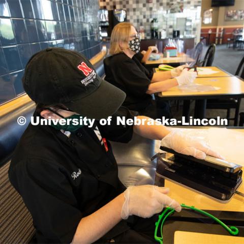 Dinning Services employees, Rochan Pinho, Janet Nichols and Dami Olsen, assemble face shields at Harper Dining Center. Once school starts up, they will use the shields for prevention of the spread of COVID-19. April 28, 2020. Photo by Gregory Nathan / University Communication.