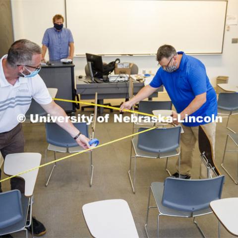 Jack Dohrman, Interim University Space Manager, with Facilities Management and Planning, and Shawn Languis, Space Planning/GIS Data Coordinator with Facilities Management and Planning use tape measures to gauge physical distancing needs within an Avery Hall classroom. Based on their measurements, seating in this classroom will shift from 35 desks in a regular semester to 14 in the fall. The change allows the university meet the six-foot social distancing needs related to COVID-19. In large lecture halls, seating capacity is expected to be reduced to 20 percent. Keith Derickson, Academic Technologies Support Manager, stands in the instructor position. A group is physically measuring every classroom on campus to see if computer-aided predictions are correct. June 1, 2020. Photo by Craig Chandler / University Communication.