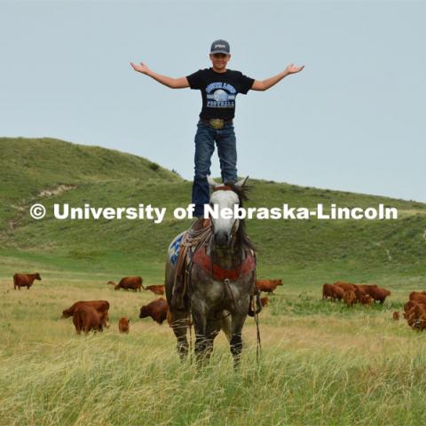 A young rancher shows his skills of standing on the back of his horse. Cattle and livestock on the Diamond Bar Ranch north of Stapleton, NE, in the Nebraska Sandhills. June 23, 2020. Photo by Natalie Jones.  Photos are for UNL use only.  Any outside use must be approved by the photographer.