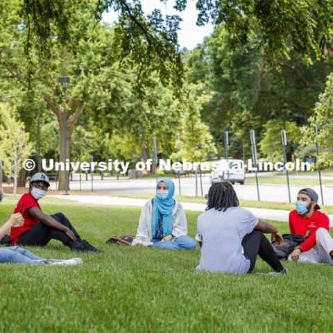 A group of students wearing masks and practice social distancing hangout under a tree on City Campus. Photo shoot of students wearing masks and practicing social distancing. June 24, 2020. Photo by Craig Chandler / University Communication
