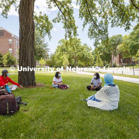A group of students wearing masks and practice social distancing hangout under a tree on City Campus. Photo shoot of students wearing masks and practicing social distancing. June 24, 2020. Photo by Craig Chandler / University Communication