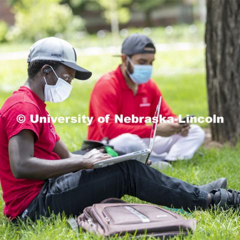 Mark Iradukunda works on his laptop and Aldi Airori checks his phone while wearing masks and practicing social distancing outdoors. Photo shoot of students wearing masks and practicing social distancing. June 24, 2020. Photo by Craig Chandler / University Communication.