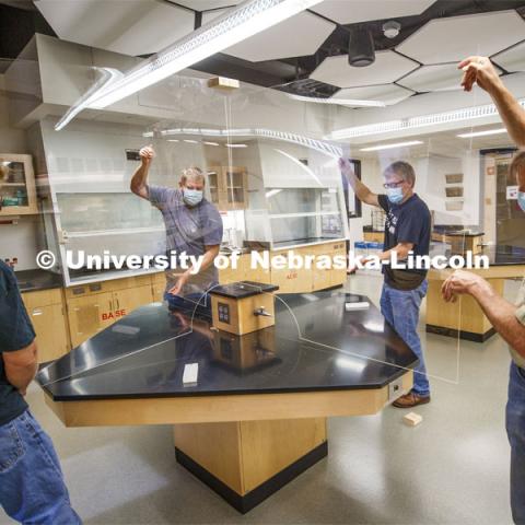 Nebraska's (from left) Mark Thompson, Keith Placek, Jody Redepenning and Pat Pribil lift an acrylic barrier onto a lab table in Hamilton Hall. The barrier is a prototype that is being refined as part of the university’s preparations for a return to on-campus instruction for the fall semester. The barriers will allow chemistry lab tables to be divided into four sections. The barrier is the second prototype and will be refined as part of 78 barriers being manufactured for the beginning of fall classes. Redepenning is chair and professor of chemistry. Thompson, Placek and Pribil are part of the university's Chemistry/Physics and Astronomy Instrument Shop. July 1, 2020. Photo by Craig Chandler / University Communication.