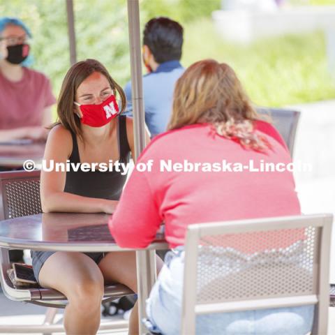 Students socialize on the patio outside the Willa Cather Dining Complex. Photo shoot of students wearing masks and practicing social distancing in dining services in Willa Cather Dining Center. July 1, 2020. Photo by Craig Chandler / University Communication.