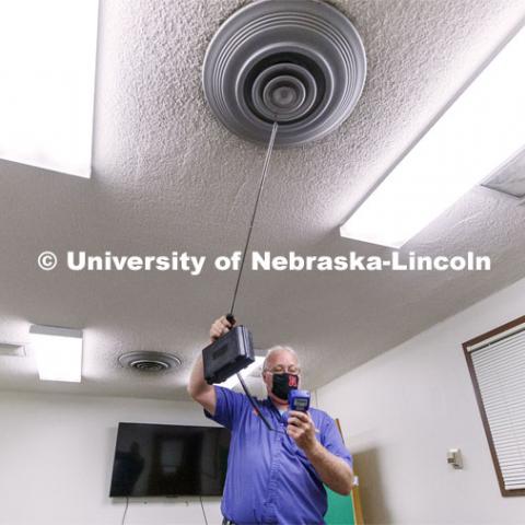 Dave Tyler, Control Systems Tech, uses a hot wire anemometer to measure air coming from a vent in a practice room in Westbrook Music Building. To mitigate the risk of virus transfer within the buildings, the facilities team is increasing by nearly 50 percent the amount of fresh air being drawn into HVAC systems. They are also upgrading filters to more efficiently capture and reduce large and small particles in the air. July 27, 2020. Photo by Craig Chandler / University Communication.