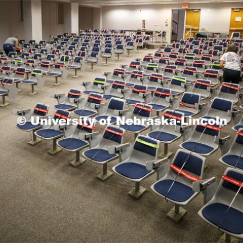 The marking crew works through the Louise Pound Hall lecture hall marking available and unavailable seats. The bands are flexible, so they do not need to be removed when the student sits down. Crews are marking classroom seats in Louise Pound Hall as part of preparing the campus for Forward to Fall. A crew is going room-to-room marking the where to sit and where the chairs/tables go. By Friday, they hope to have 483 classrooms and 8970 seats on all campuses marked and ready. August 3, 2020. Photo by Craig Chandler / University Communication.