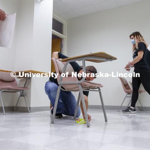 Scott Plautz places a seat available sticker on the floor under a desk. The stickers allow the seats to be moved by the janitorial crew for cleaning and be placed back in the correct spots. Crews mark classroom seats in Louise Pound Hall as part of preparing the campus for Forward to Fall. A crew is going room-to-room marking the where to sit and where the chairs/tables go. By Friday, they hope to have 483 classrooms and 8970 seats on all campuses marked and ready. August 3, 2020. Photo by Craig Chandler / University Communication.