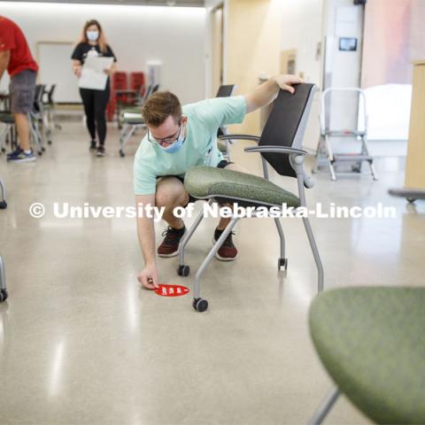 Student worker Alex Cathcart places a seat-available sticker marking in the computer lab of the Johnny Carson Emerging Media Center. Crews mark classroom seats as part of preparing the campus for Forward to Fall. A crew is going room-to-room marking the where to sit and where the chairs/tables go. By Friday, they hope to have 483 classrooms and 8970 seats on all campuses marked and ready. August 3, 2020. Photo by Craig Chandler / University Communication.