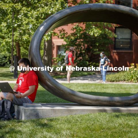 Photo shoot of students on city campus display mask wearing and social distancing. A young man sits and studies by the Fragment XO Sculpture as students cross campus near by.August 5, 2020. Photo by Craig Chandler / University Communication.