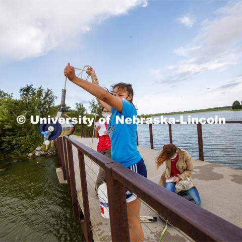 Malayna Wingert, a sophomore from Sterling, NE, lifts a water sample out of Holmes Lake as Anni Poetz and Maddie Carpenter record data. UCARE students of Professor Jessica Corman take water samples at Holmes Lake. The project is to see what makes the local lakes turn green. Is it an influx of nutrients from rain? Warm weather in the summer? They are testing what nutrients promote growth of algae and cyanobacteria in the lake, and they are testing this throughout the year. August 10, 2020. Photo by Craig Chandler / University Communication.