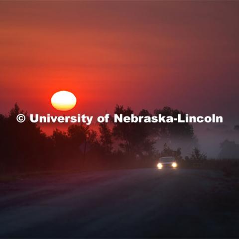 A car drives up out of the fog on a rural Nebraska road as the sun rises in the early morning sky. September 15, 2020. Photo by Craig Chandler / University Communication.