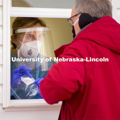 Bria Foley, senior in pre-med and a student worker for the saliva testing, hands the package of vial, straw and alcohol wipe to a walk-up tester Tuesday morning. Saliva testing at East Stadium loop site. January 19, 2021. Photo by Craig Chandler / University Communication.