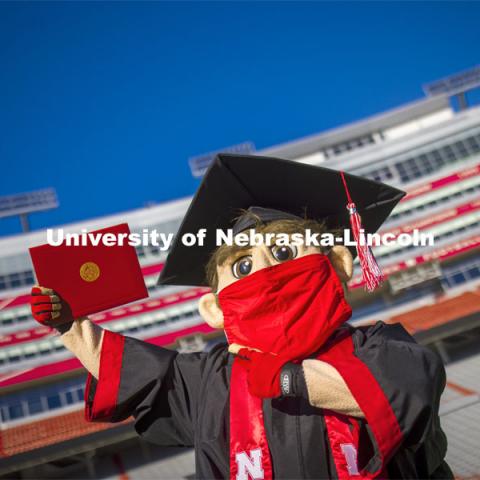 A masked Herbie Husker holding a diploma, poses in regalia to announce spring commencement will be in Memorial Stadium. March 1, 2021. Photo by Craig Chandler / University Communication.